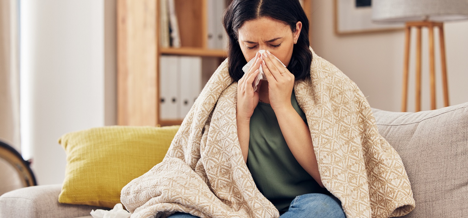 woman sitting on couch blowing nose with tissue